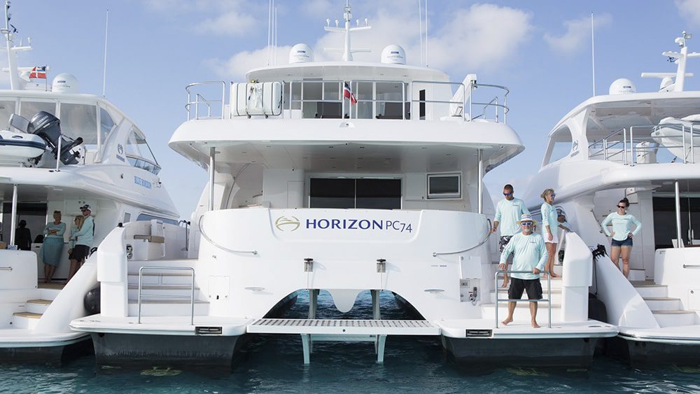 A group of people standing next to a group of white motor yachts.
