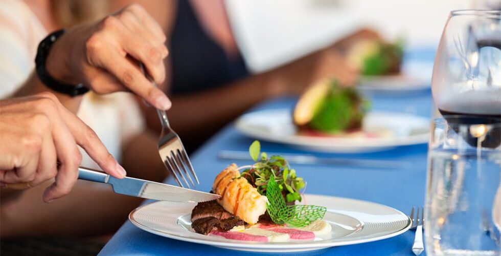 Person dining at a luxury restaurant on board a power catamaran charter, cutting into an elegantly plated dish.