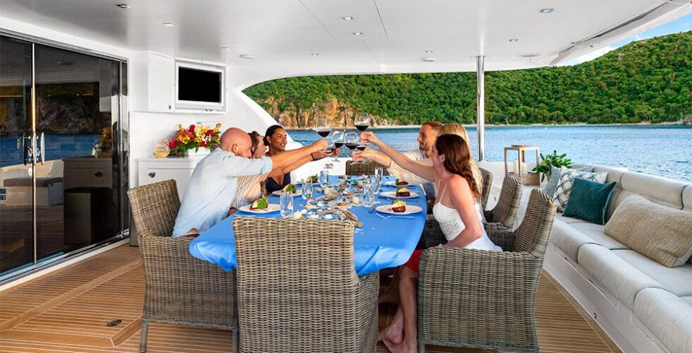 Group of friends enjoying a meal and toasting drinks on the deck of a luxury power catamaran yacht.