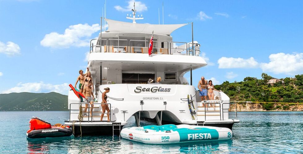 Group of people enjoying leisure time on and around a luxury power catamaran charter anchored in clear blue waters.
