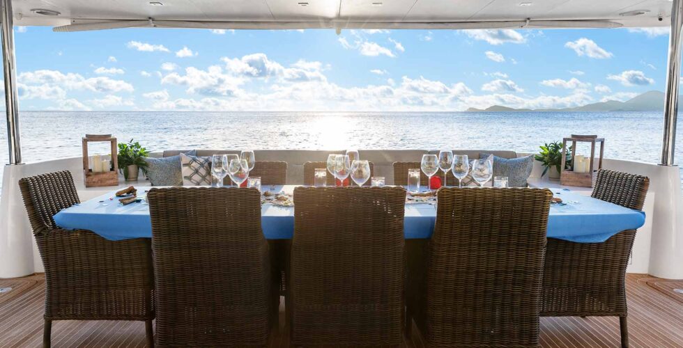 Dining setup on a luxury power catamaran charter deck with a view of the sea and horizon.
