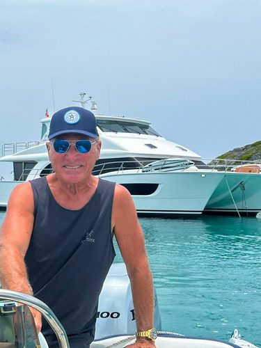 Man in cap steering boat near yacht.